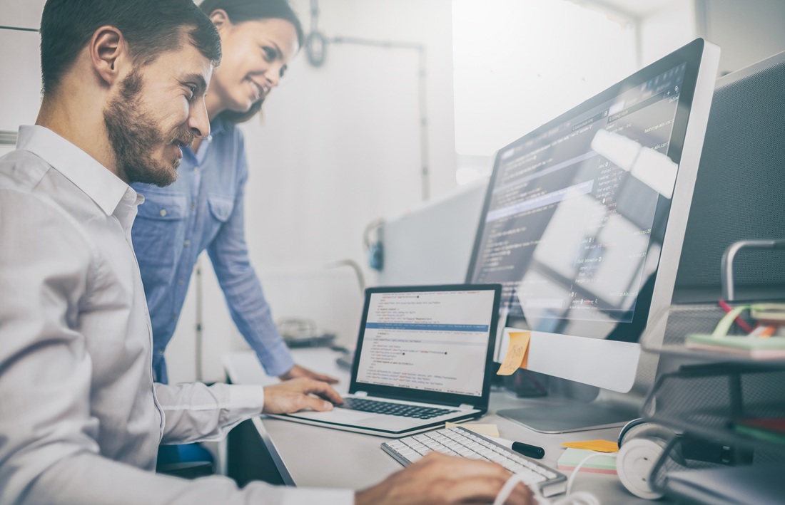 a focused male programmer types away at his keyboard, while a supportive female colleague observes with a smile