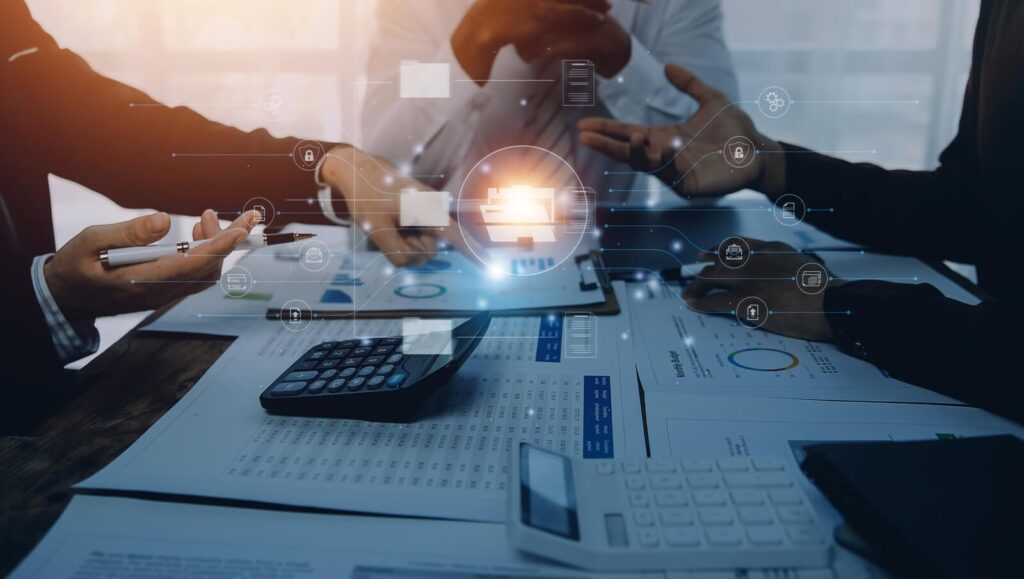 a group of professionals engage in a lively discussion around a table filled with financial documents and digital devices
