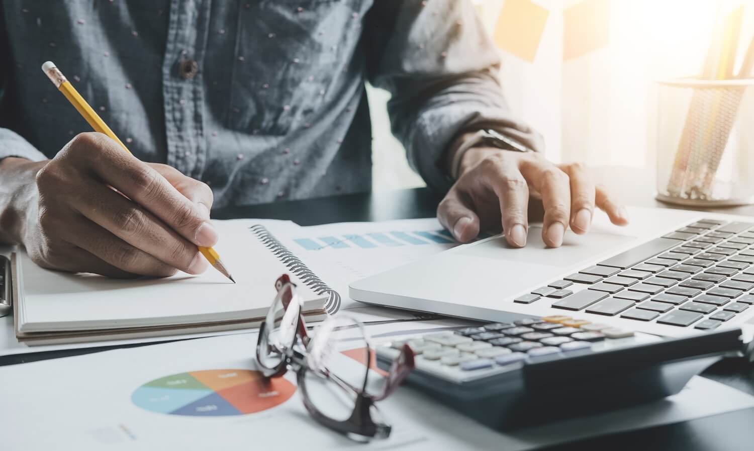 businessman or accountant hand holding pen working making notes and using laptop computer to calculate business data