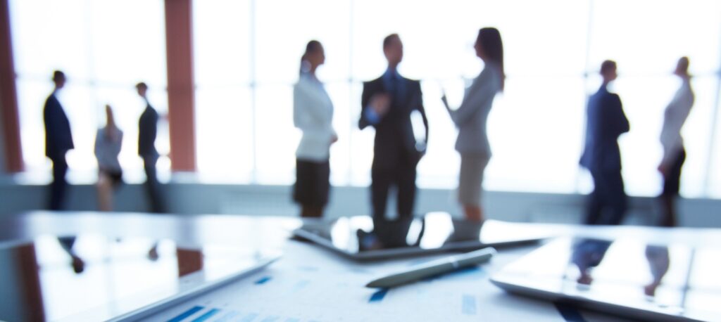 Close-up of business document in clipboard at workplace on background of office workers interacting