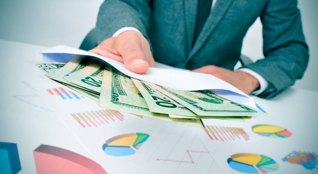 man wearing a suit sitting in a desk giving an envelope full of dollar bills
