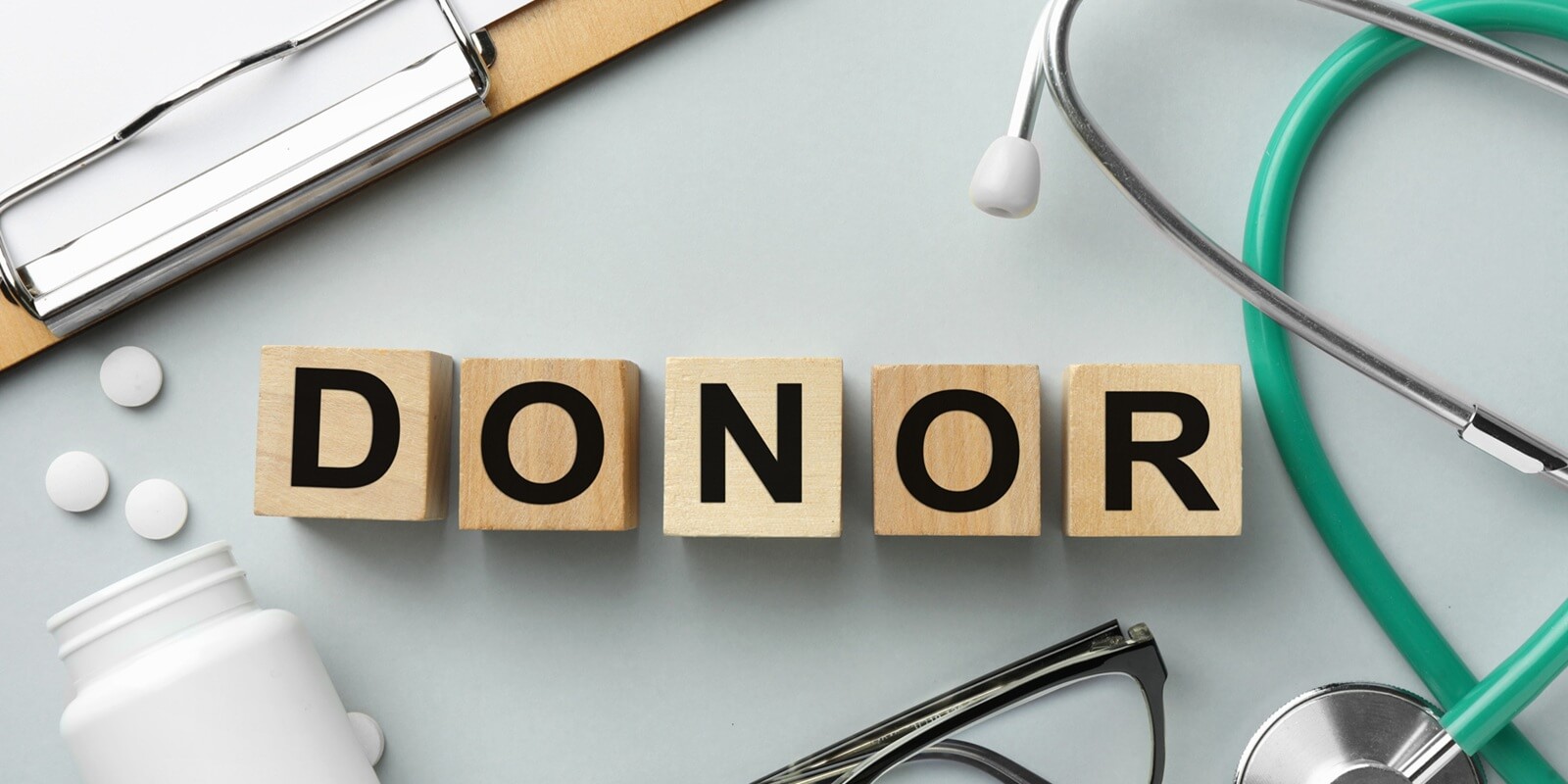 donor trust cybersecurity- word donor made of wooden cubes, clipboard, stethoscope, glasses and pills on light gray table, flat lay