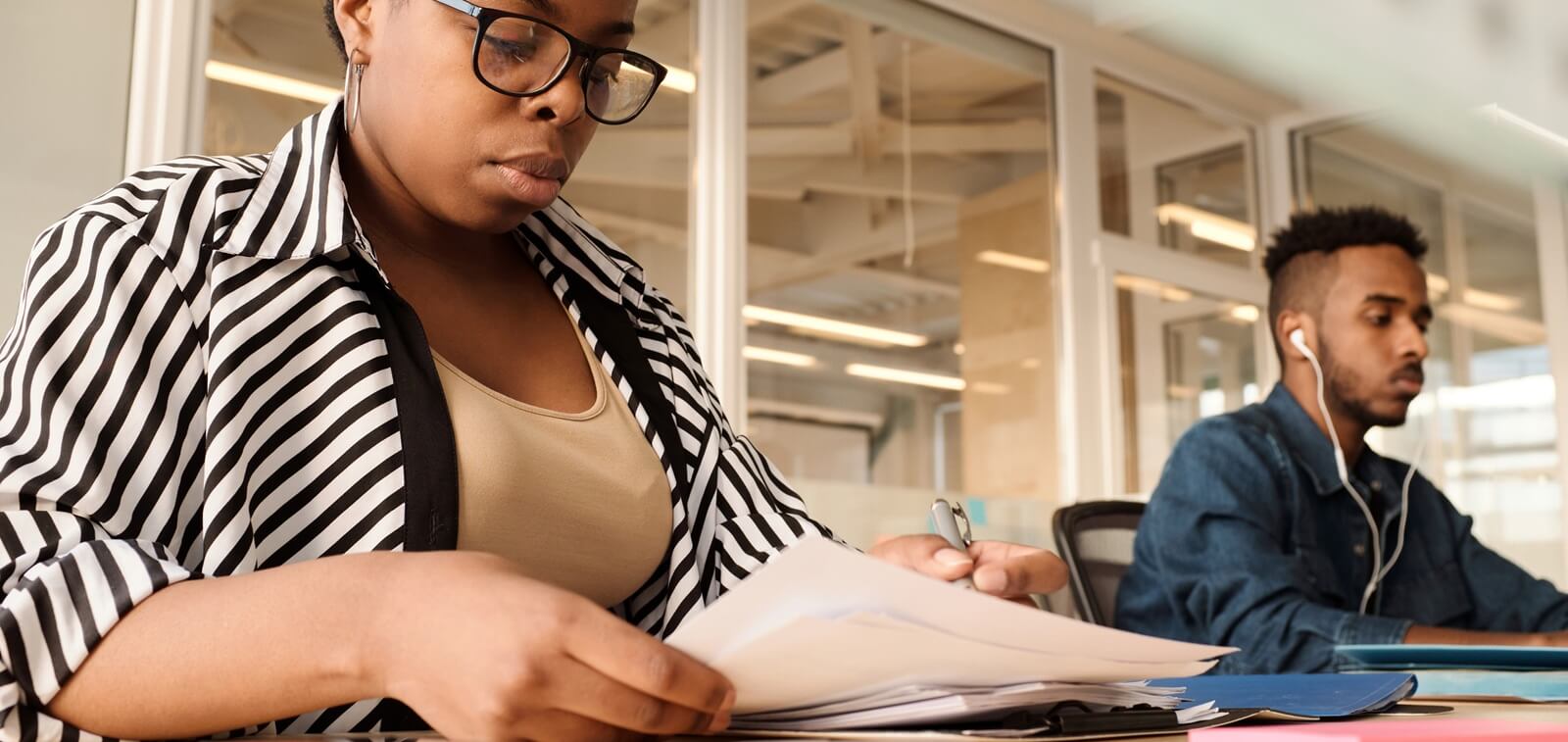 low angle view of black woman working with papers in modern office, young man in earphones using computer beside