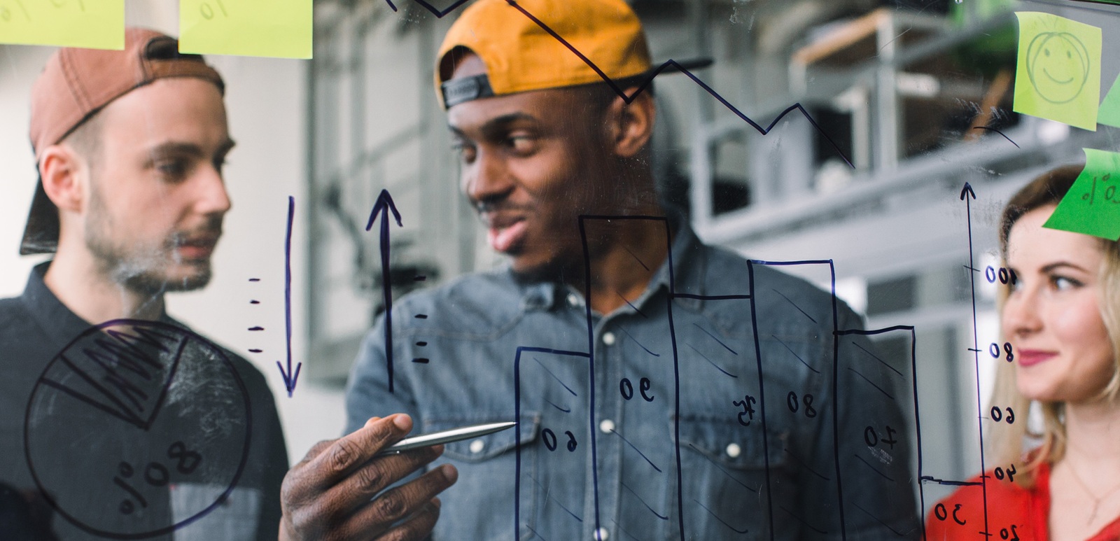 creative group of three multiethnical business people freelancers brainstorming on glass wall in office