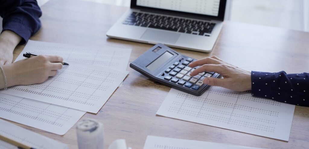 accountants or auditors reviewing financial documents while using laptop, calculator and sitting opposite one another at the wooden desk in office