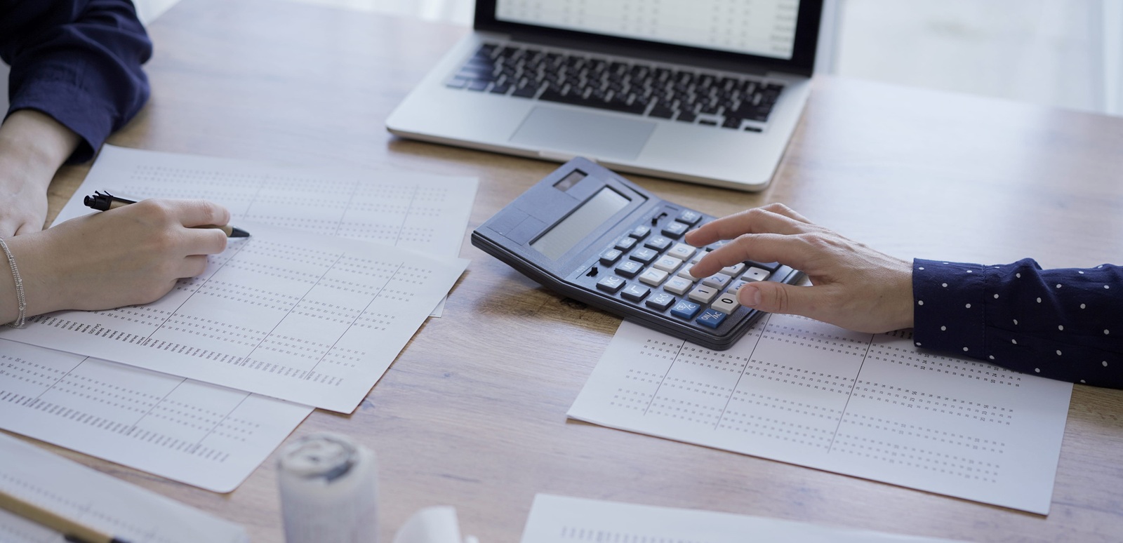 accountants or auditors reviewing financial documents while using laptop, calculator and sitting opposite one another at the wooden desk in office