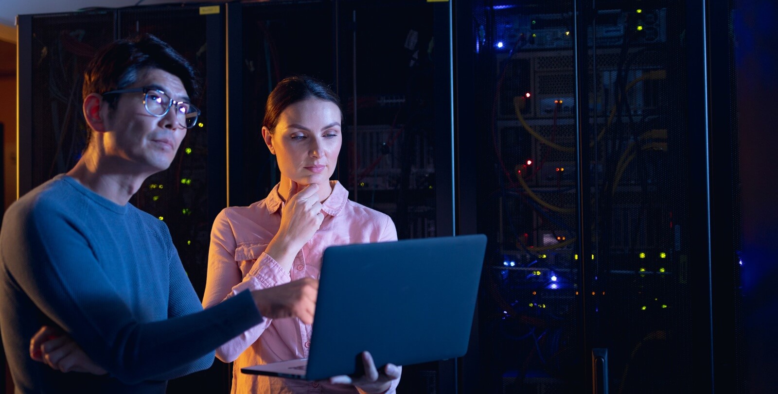 male and female engineers using laptop in computer server room. database server management and maintenance concept
