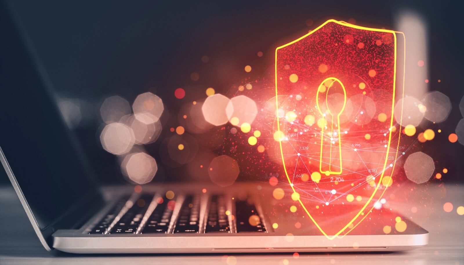 Shield hologram with keyhole over laptop on desk, glowing in orange light against blurred background