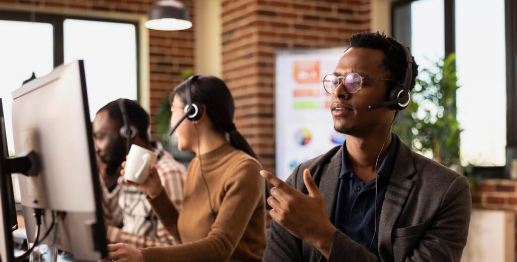 african american male employee in modern workspace, listening attentively through a headset while assisting a client
