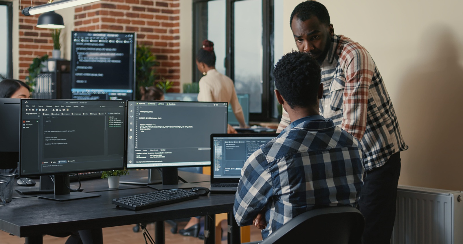 software developer writing code on laptop and computer keyboard looking at multiple screens with programming language is interrupted by coworker asking for advice