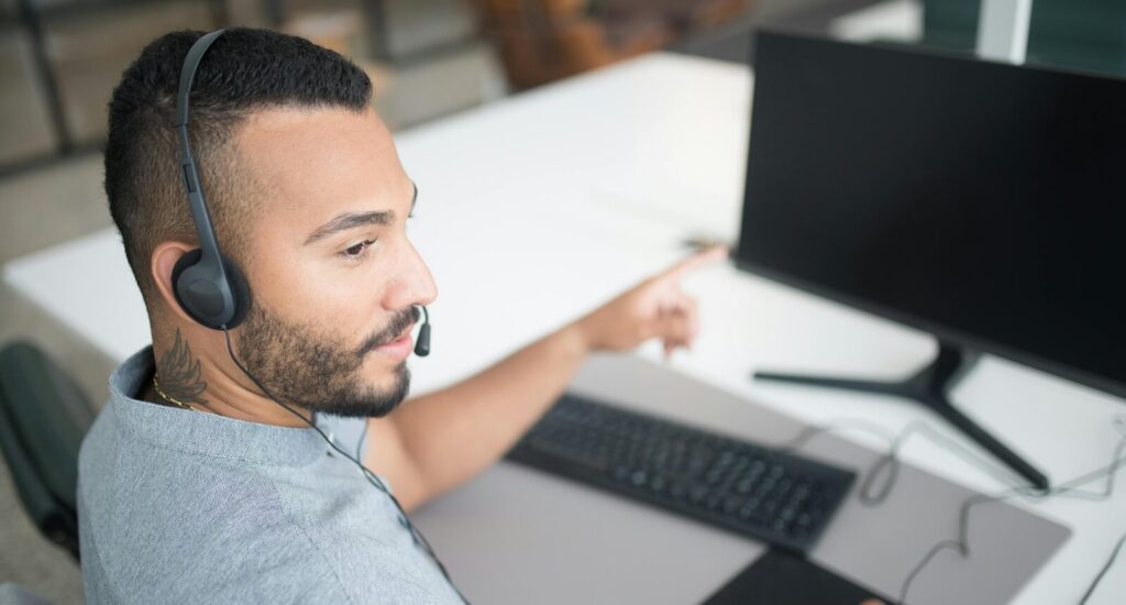 bearded man in gray shirt wearing black headset using computer