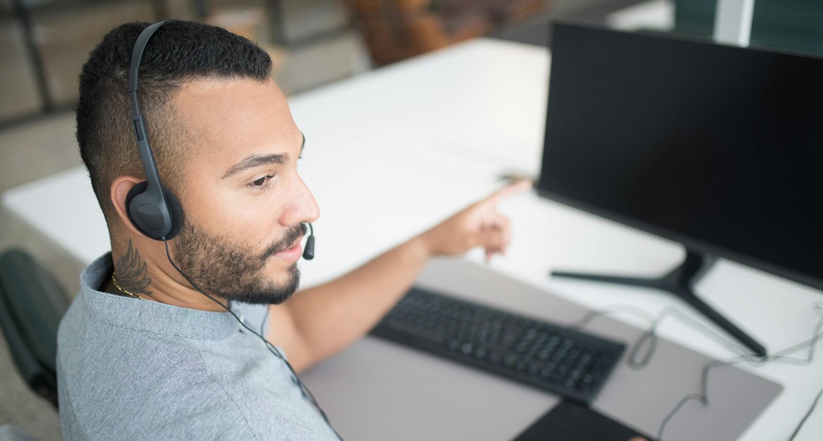 bearded man in gray shirt wearing black headset using computer
