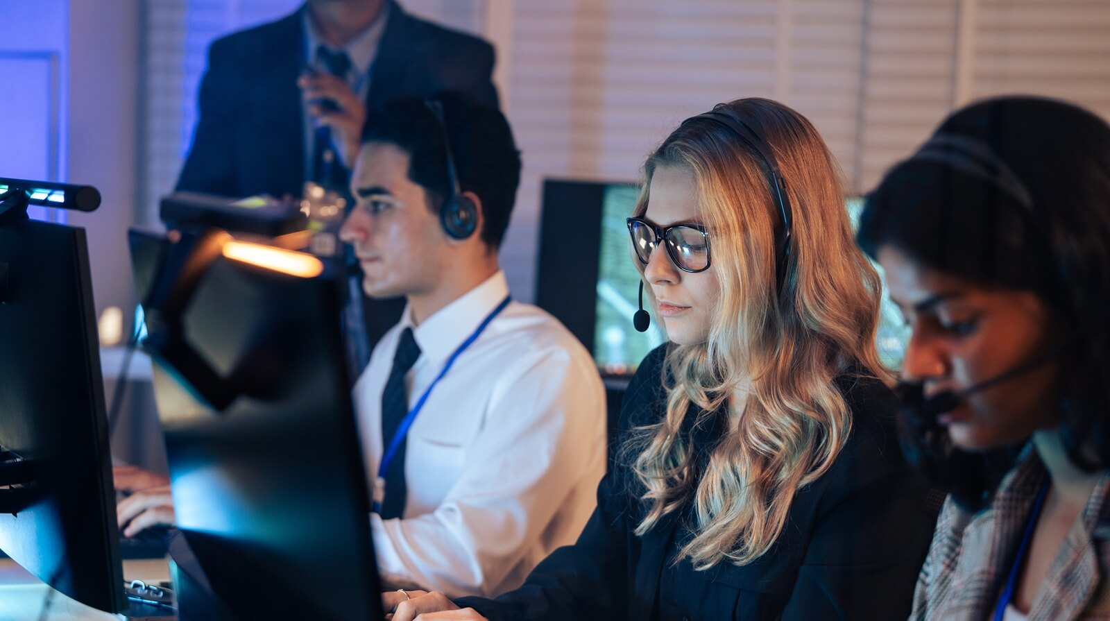 dedicated customer service agents works on computers with headsets in a dark office