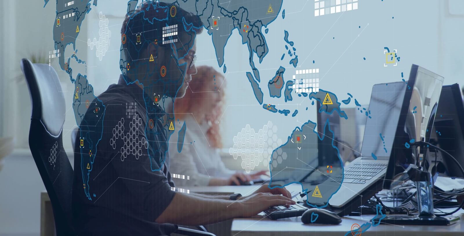 monitoring two IT analysts in shirts scanning alerts in office, with monitors world map overlay