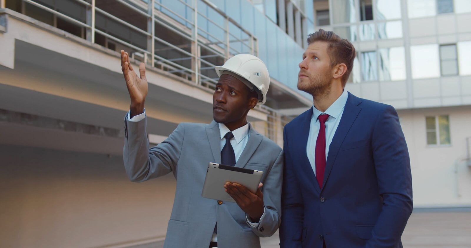 professionals assess the construction site, with one pointing out details and the other taking notes