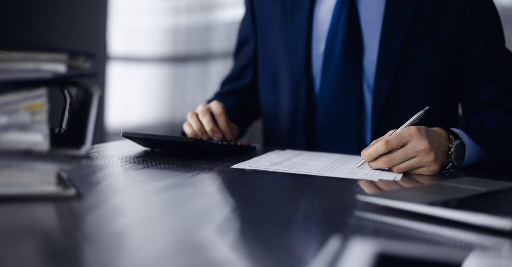 unknown man accountant in blue blazer use calculator and computer with holding pen on while staying at home during covid pandemic