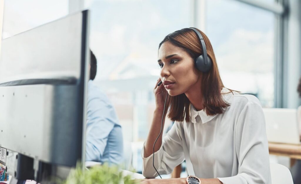 focussed young businesswoman wearing a headset while talking to client on the phone and working on a computer in the office