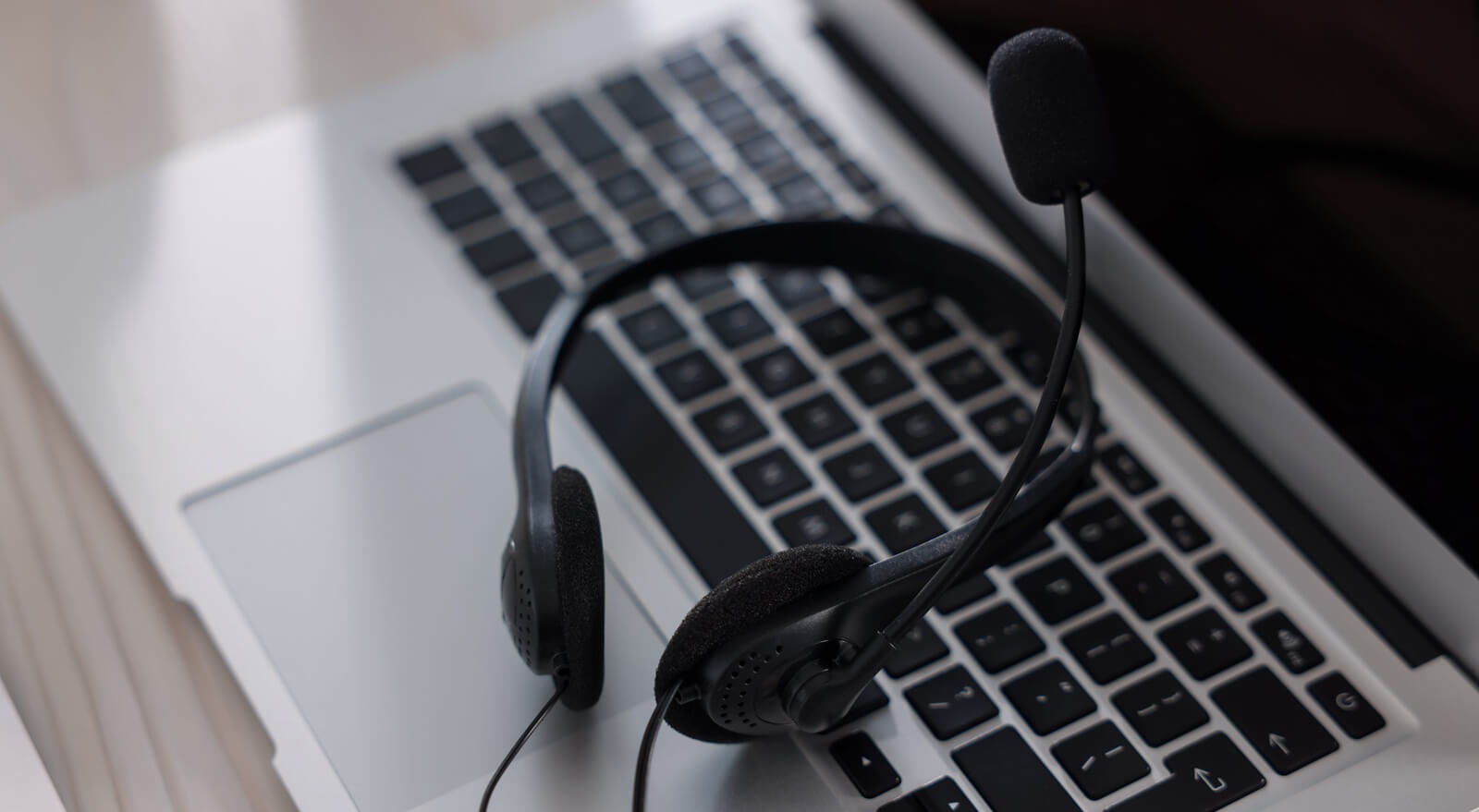 headset with microphone and laptop on white wooden desk in office, closeup